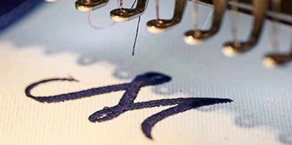 Close-up of embroidery machine stitching a blue letter on fabric.