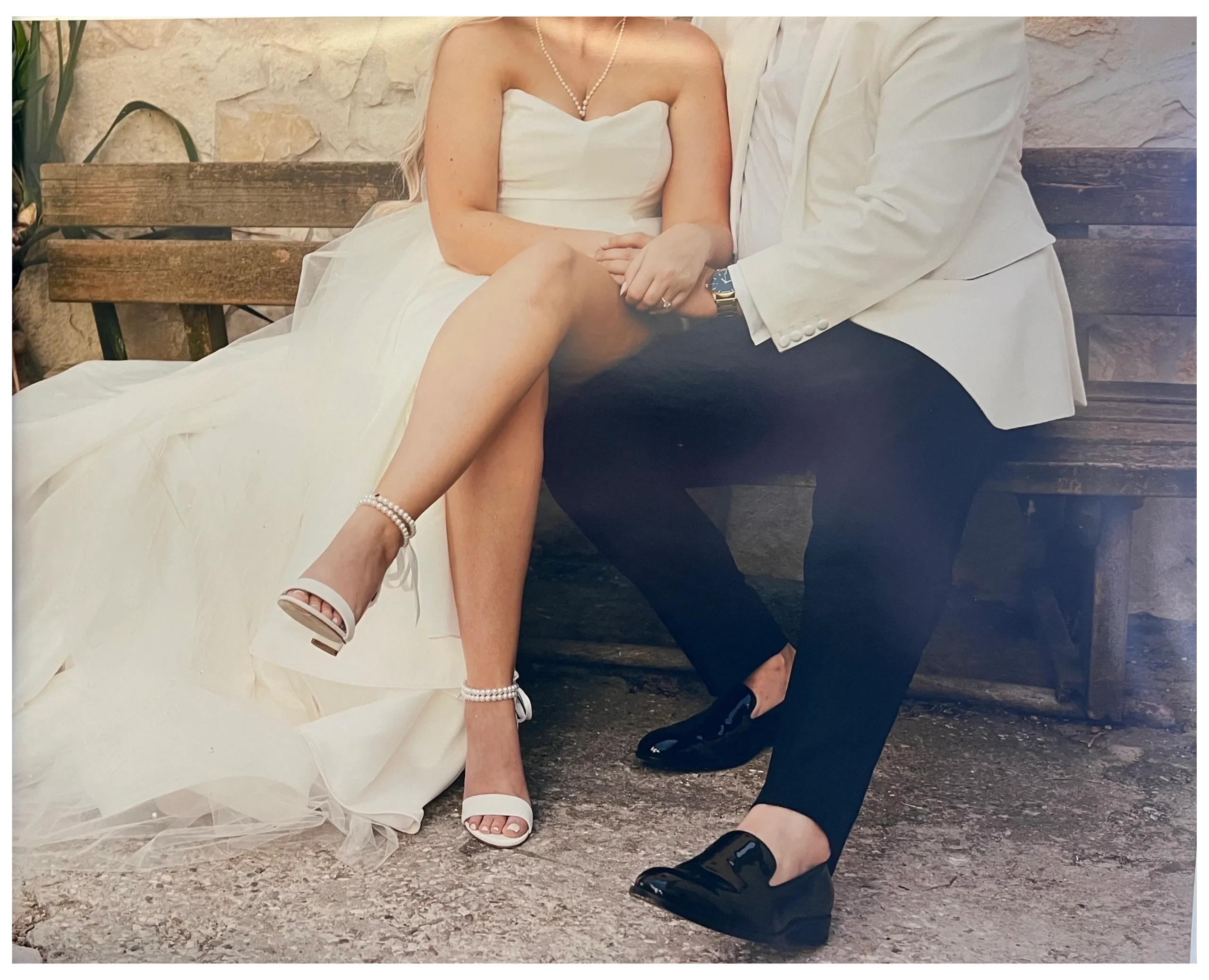 Bride and groom holding hands, seated on a rustic bench.